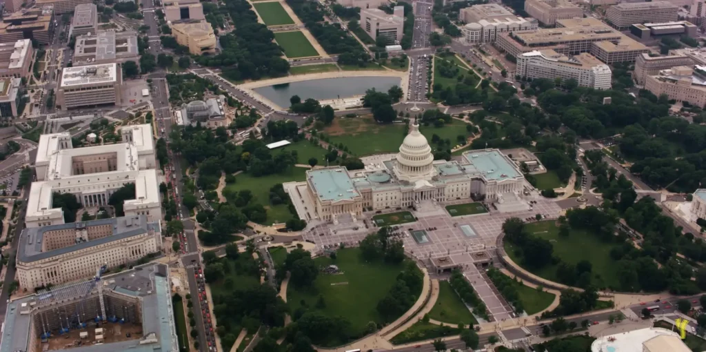 Aerial view of the United States Capitol Building surrounded by lush green gardens and streets, offering a bird's-eye perspective of Washington, DC.